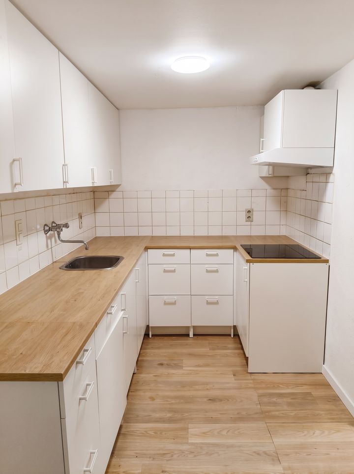Renovated white U-shaped kitchen with wooden worktop and white wall tiles
